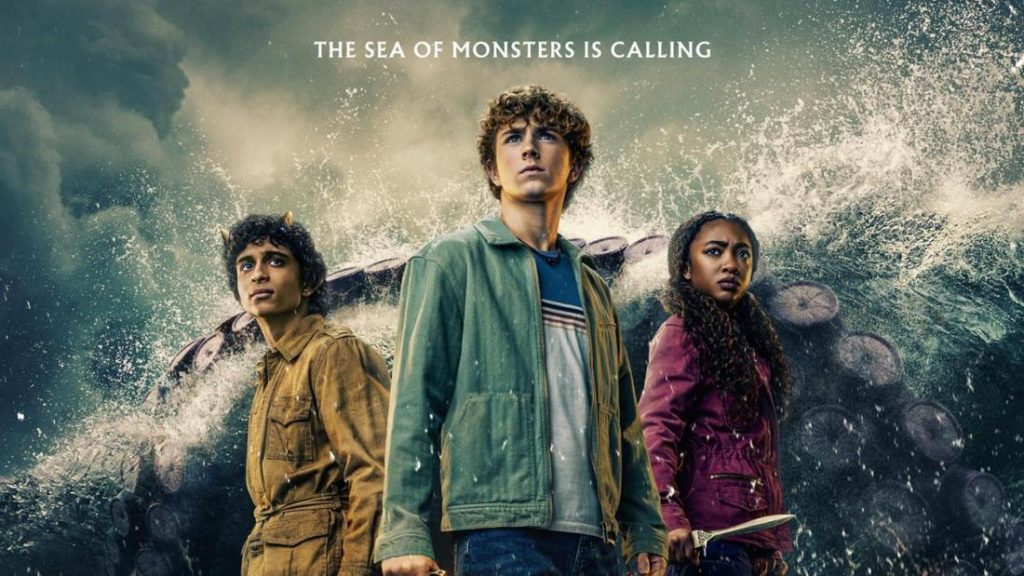 Ein Filmplakat zeigt drei Jugendliche vor einer dramatischen Szene mit stürmischem Meer und riesigen Tentakeln. In der Mitte steht ein Junge mit lockigem braunem Haar und blauen Augen, bekleidet mit einer khakifarbenen Jacke und einem gestreiften Hemd, der entschlossen nach oben blickt. Links von ihm steht ein Junge mit brauner Haut, der ein braunes Hemd und goldene Hörner trägt, und nach links oben schaut. Rechts von ihm steht ein Mädchen mit dunkler Haut und dunklen, lockigen Haaren, das eine dunkelrote Jacke trägt und ebenfalls nach oben schaut. Über ihnen steht in Großbuchstaben der englische Text "THE SEA OF MONSTERS IS CALLING".