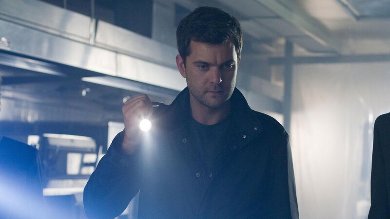 Ein Mann in einer dunklen Jacke leuchtet mit einer Taschenlampe in einer schwach beleuchteten Umgebung.