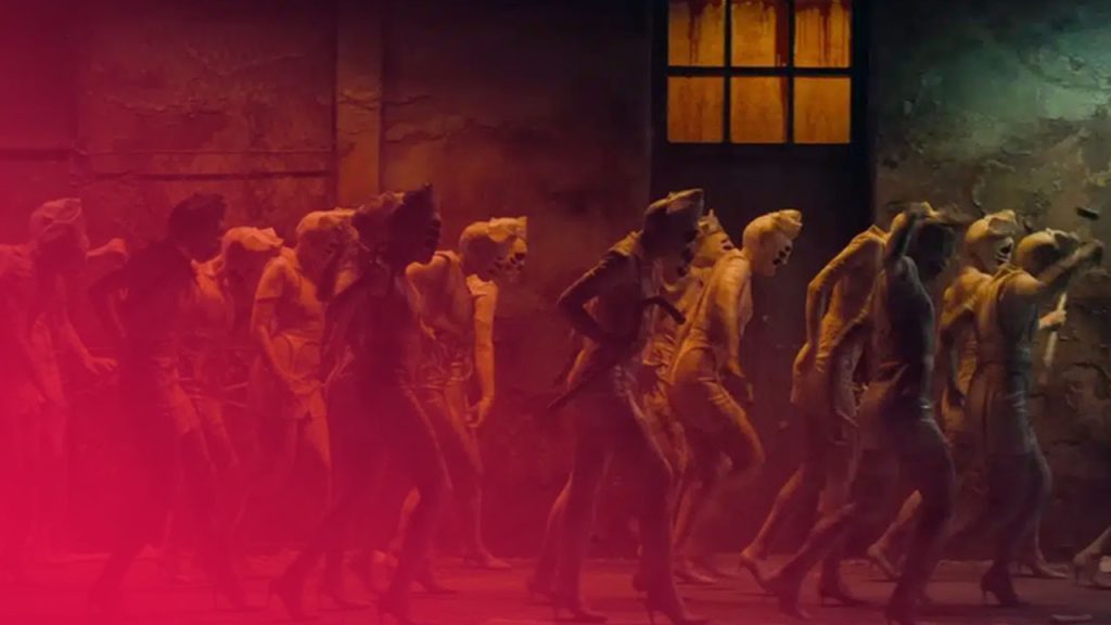 Gruppe von Frauen in Uniformen und High Heels geht in einem dunklen, schmutzigen Korridor mit einem beleuchteten Fenster.