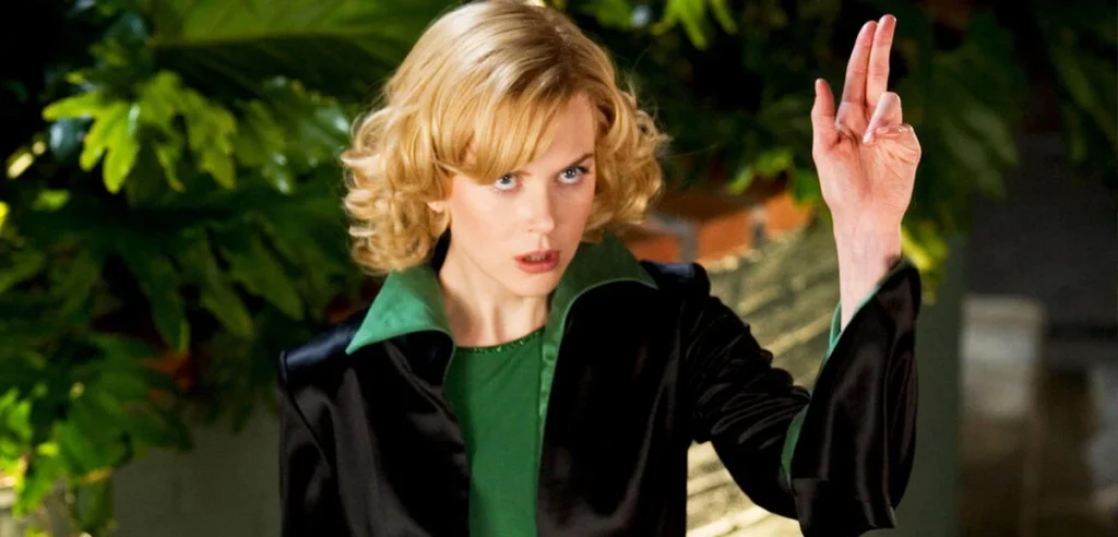 Halbaufnahme von Nicole Kidman in einer schwarzen Jacke mit grünem Kragen, die mit ernstem Blick die Hand erhebt.