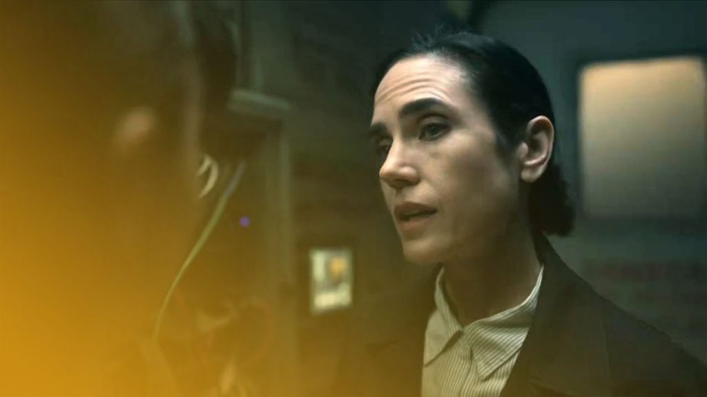 Eine Frau mit dunklen Haaren, ein hell gestreiftes Hemd und einen schwarzen Blazer tragend, redet mit einer anderen Person in einem dunklen Raum mit elektronischer Ausrüstung.