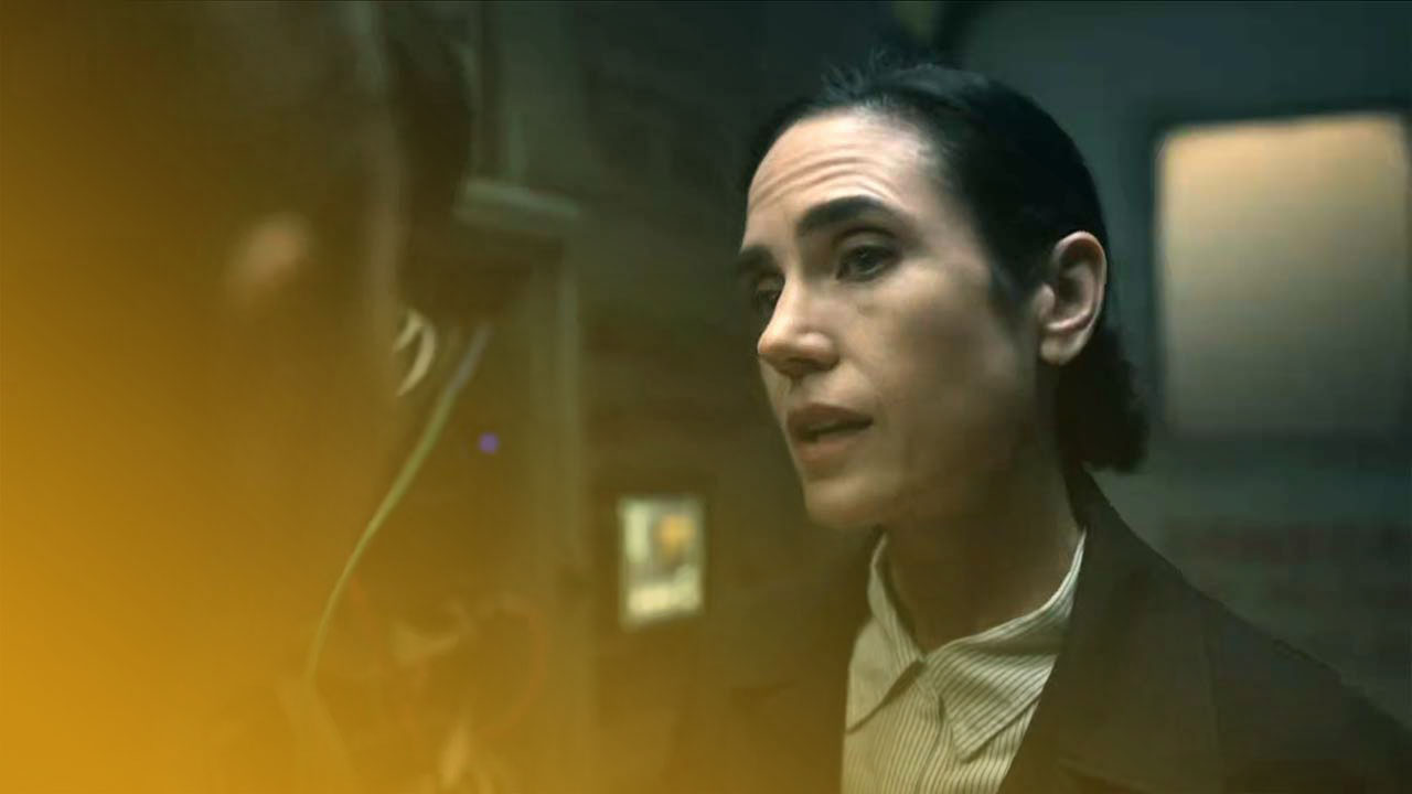 Eine Frau mit dunklen Haaren, ein hell gestreiftes Hemd und einen schwarzen Blazer tragend, redet mit einer anderen Person in einem dunklen Raum mit elektronischer Ausrüstung.