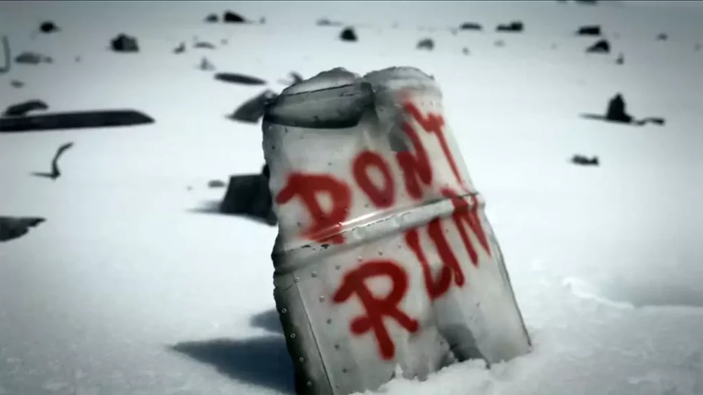 Metallstück im Schnee mit roter Aufschrift "DON'T RUN". Verschneite, trübe Landschaft im Hintergrund.