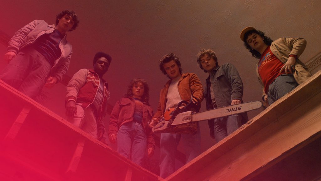 Sechs Personen im 80er-Jahre-Stil stehen auf einem Dachbalken und schauen nach unten. Eine Person hält eine Kettensäge. Die Perspektive ist von unten nach oben gerichtet.