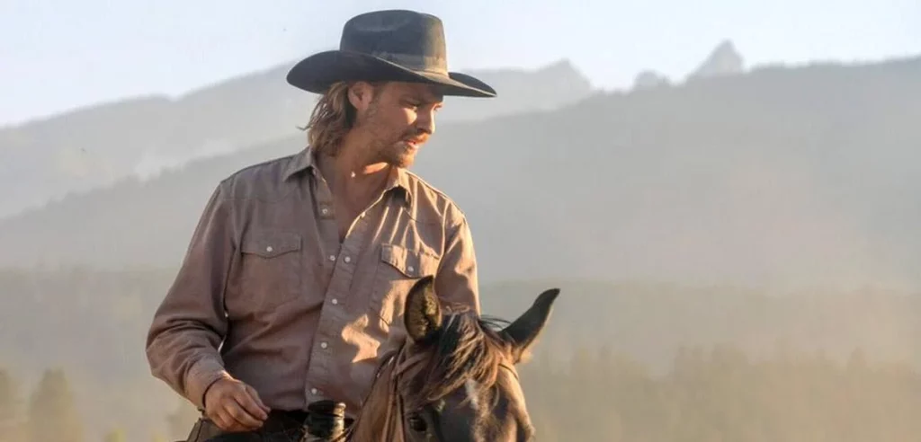 Mann mit Hut und Hemd auf einem Pferd, Blick nach rechts, bewaldete Berge im Hintergrund.