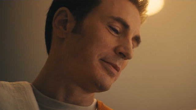 Nahaufnahme eines Mannes mit kurzem Haar, der mit einem sanften Lächeln nach unten blickt. Warme, gedämpfte Beleuchtung.