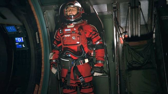 Astronaut in rotem NASA-Raumanzug mit Helm steht konzentriert in einer technologisch ausgestatteten Raumkapsel.