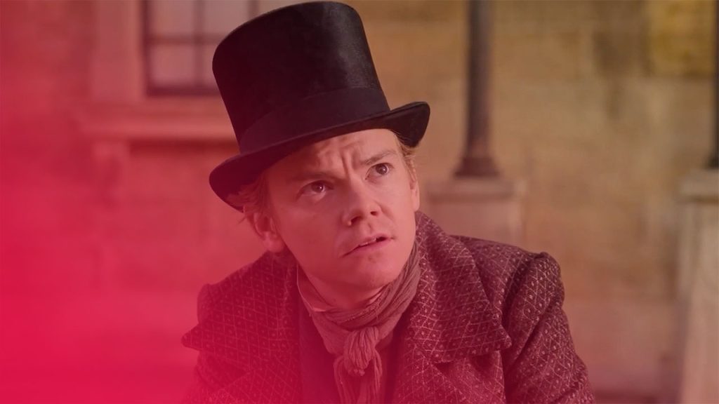 Ein Mann mit Hut und Schal blickt nach oben. Er trägt einen schwarzen Zylinder, einen gemusterten Mantel und einen grünen Schal. Der Hintergrund ist verschwommen.