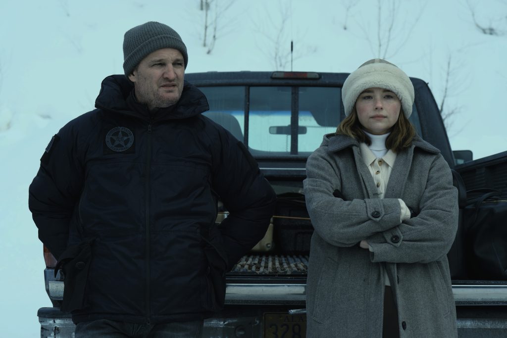 Mann in dunkler Jacke mit "US Marshal"-Patch und junge Frau in grauem Wintermantel stehen im Schnee vor einem Pickup.