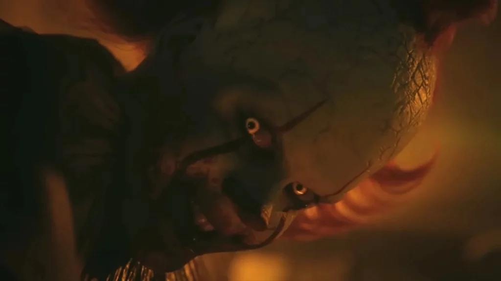 Nahaufnahme eines gruseligen Clowns mit rissiger weißer Schminkhaut, gelben Augen und rotem Haar in düsterem, warmem Licht.