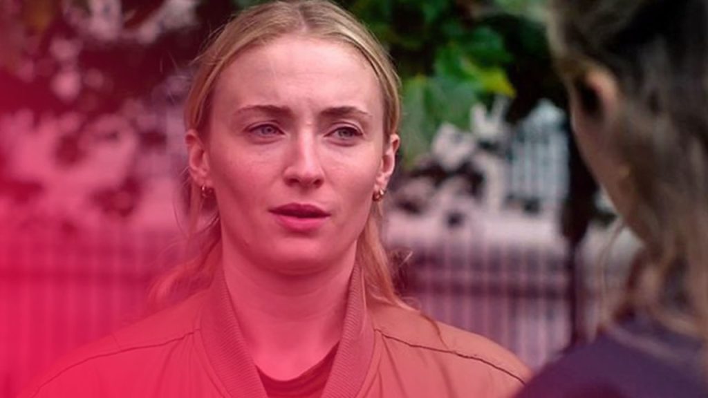 Nahaufnahme einer blonden Frau in einer beigen Bomberjacke, die mit besorgtem Blick zu einer Person außerhalb des Bildes spricht.