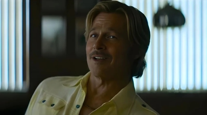 Ein hellblonder Mann mit Schnurrbart lächelt leicht in einem gelben Hemd vor einem Hintergrund mit Lamellenfenstern.