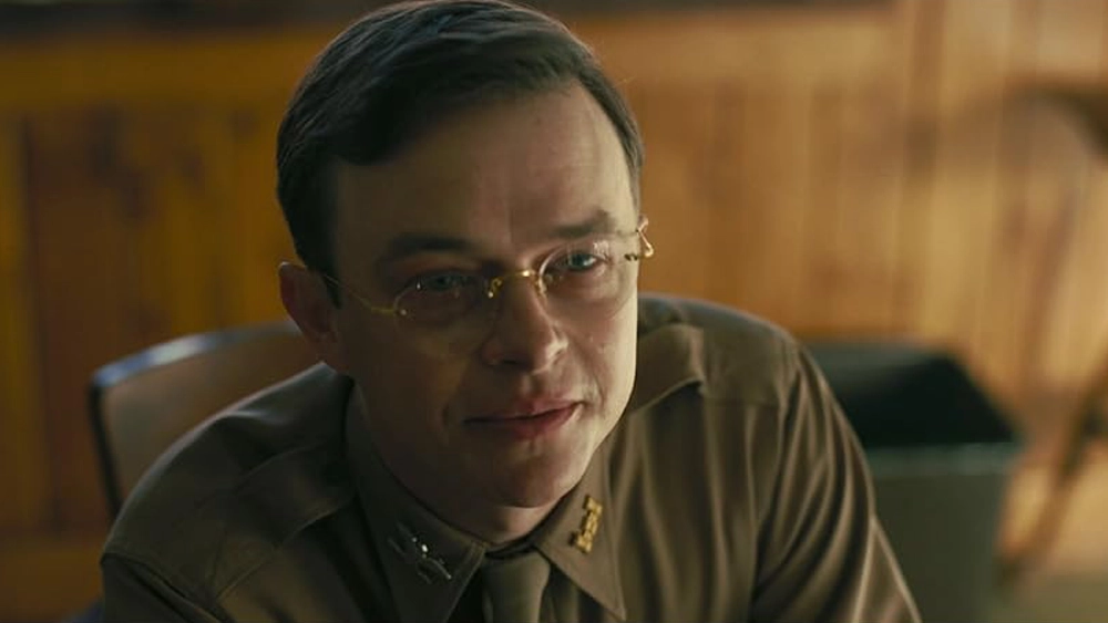 Ein Mann mit Brille in einer khakifarbenen Militäruniform blickt mit einem leichten Lächeln direkt in die Kamera.