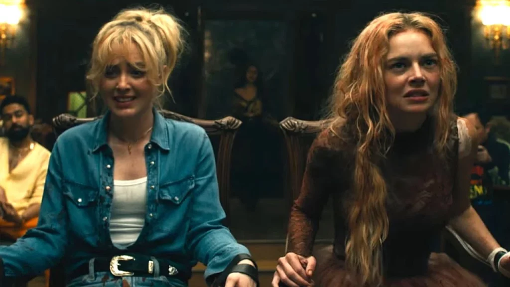 Zwei angespannte Frauen sitzen gefesselt in dunklen Stühlen. Sie blicken erschrocken nach vorn in einem düsteren Raum.