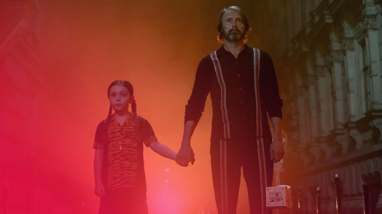 Ein Mann und ein Mädchen halten Händchen in einer nebligen, gelblich beleuchteten Straße bei Nacht.