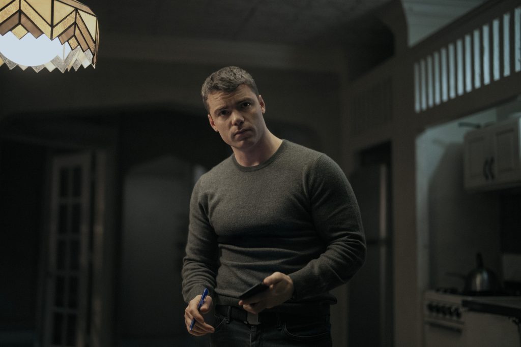 Ein Mann im grauen Pullover blickt besorgt, während er ein Smartphone und einen Stift in den Händen hält.