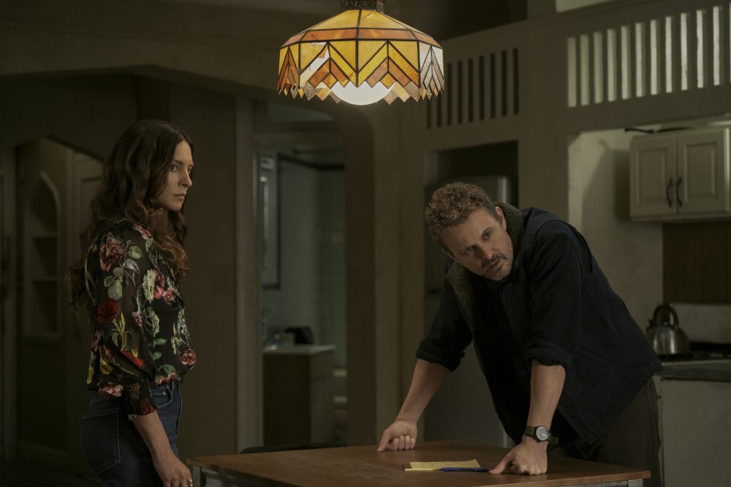 Frau und über Tisch gebeugter Mann blicken ernst in einer Küche unter einer Tiffany-Lampe.