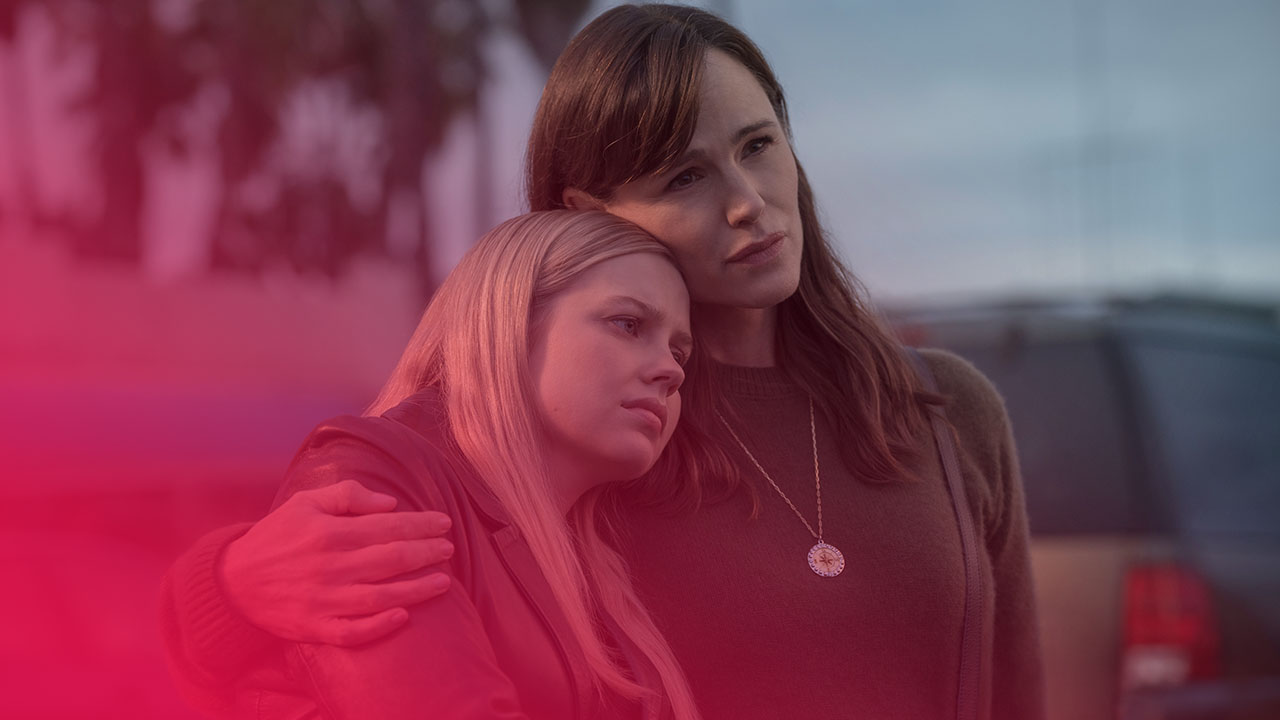 Eine braunhaarige Frau umarmt tröstend ein blondes Mädchen, das den Kopf an ihre Schulter lehnt; beide blicken ernst.