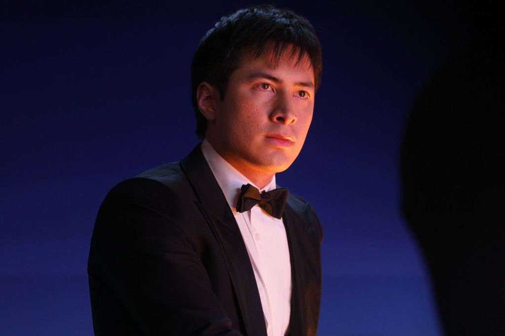 Porträt eines nachdenklichen Mannes im schwarzen Smoking mit Fliege, beleuchtet von warmem, seitlichem Licht vor blauem Grund.