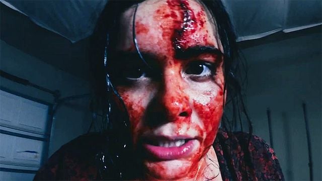 Nahaufnahme eines blutüberströmten Gesichts einer Frau, die mit schmerzverzerrtem Blick direkt in die Kamera schaut.