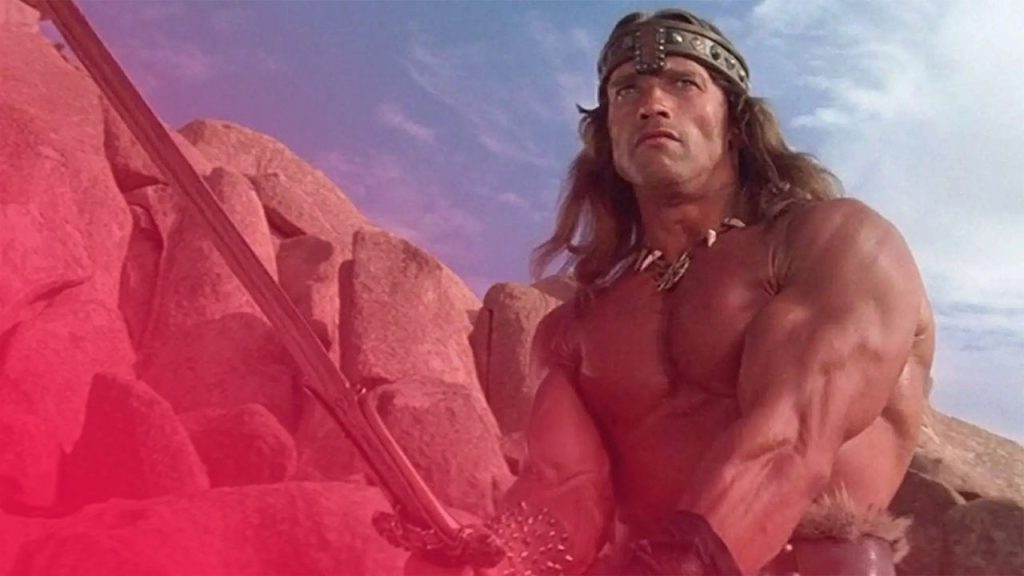 Ein muskulöser Krieger mit Stirnband hält ein Schwert vor felsigem Hintergrund und blickt entschlossen nach oben.