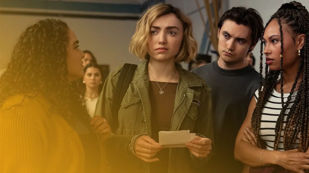 Vier junge Erwachsene stehen in einer heller beleuchteten Halle. Eine Frau mit blonden, kurzen Haaren und grüner Jacke hält einen Zettel und blickt besorgt. Links spricht eine Frau mit lockigem Haar zu ihr, rechts stehen eine Frau mit Zöpfen und ein Mann mit ernstem Gesichtsausdruck.