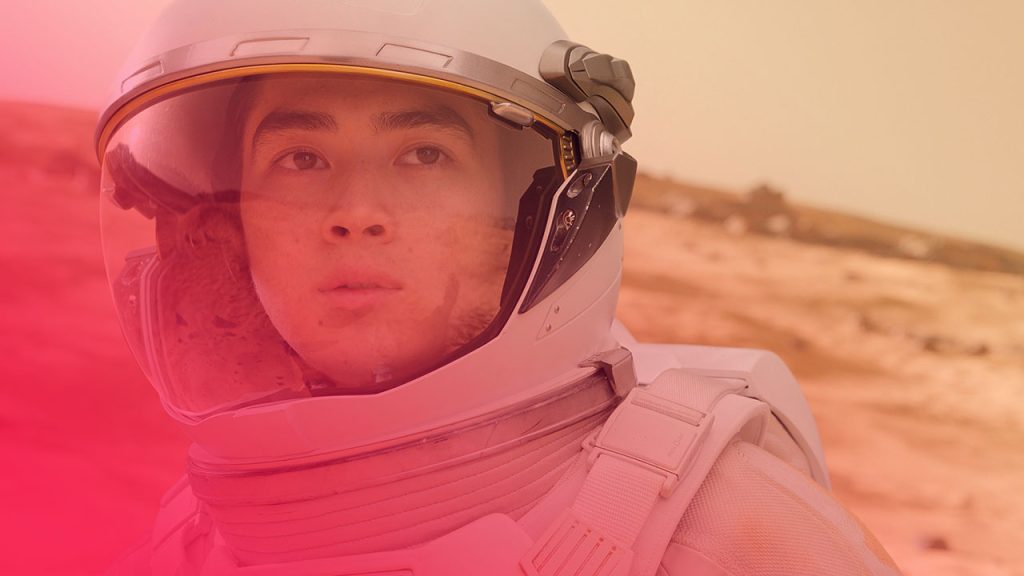 Nahaufnahme eines Astronauten in einem weißen Raumanzug mit Helm, der auf einer roten, sandigen Planetenoberfläche steht, möglicherweise dem Mars.