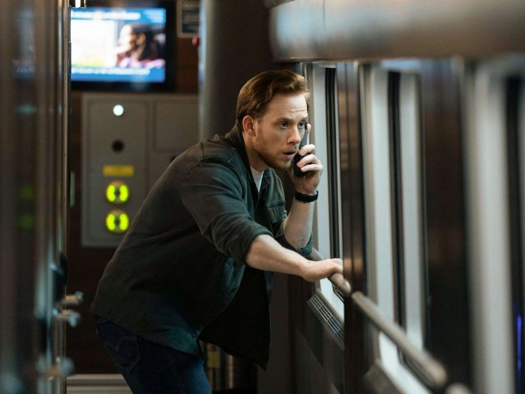 Ein besorgter Mann telefoniert in einem Zugabteil und blickt dabei angespannt aus dem Fenster.