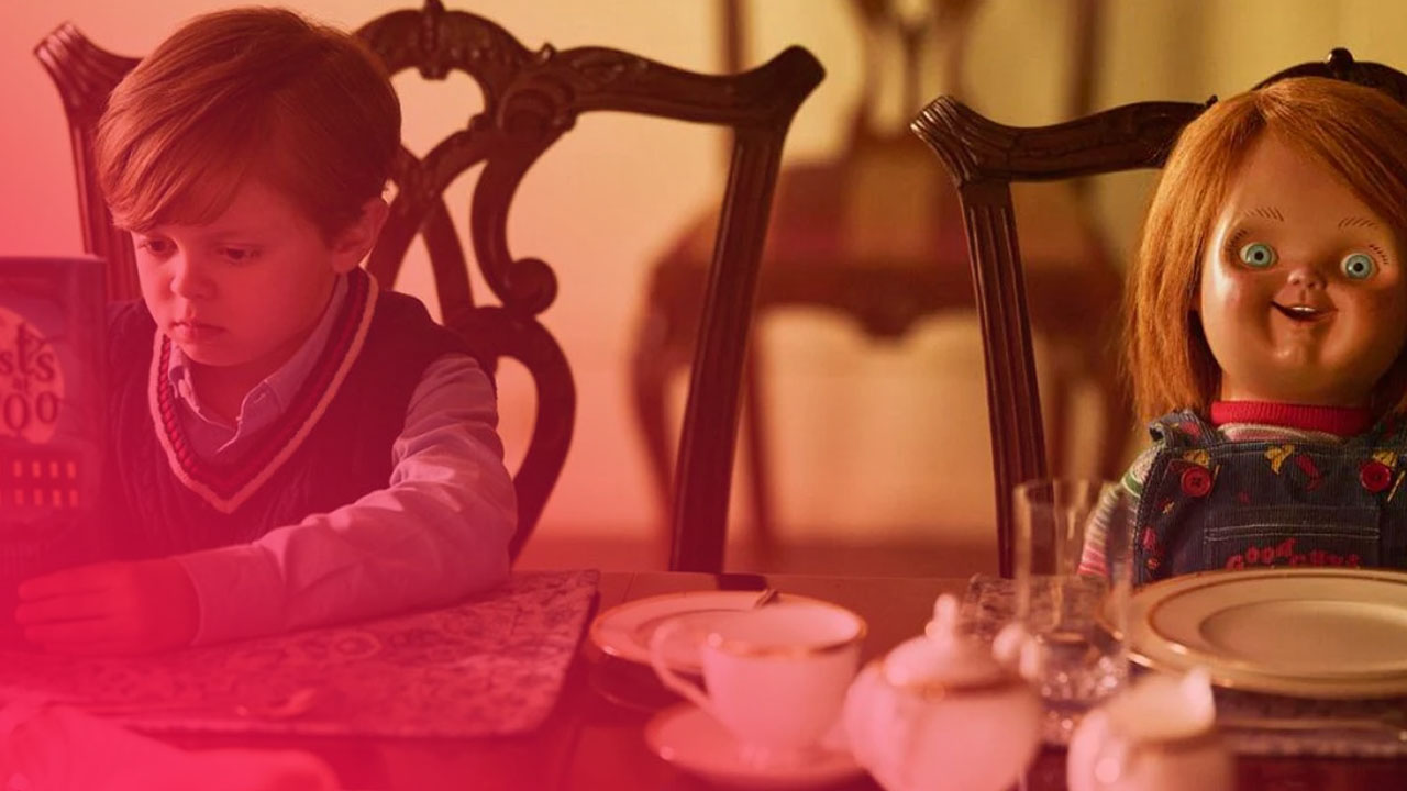 Ein kleiner Junge liest am Esstisch ein Buch, während rechts daneben die Chucky-Puppe auf einem Stuhl sitzt.