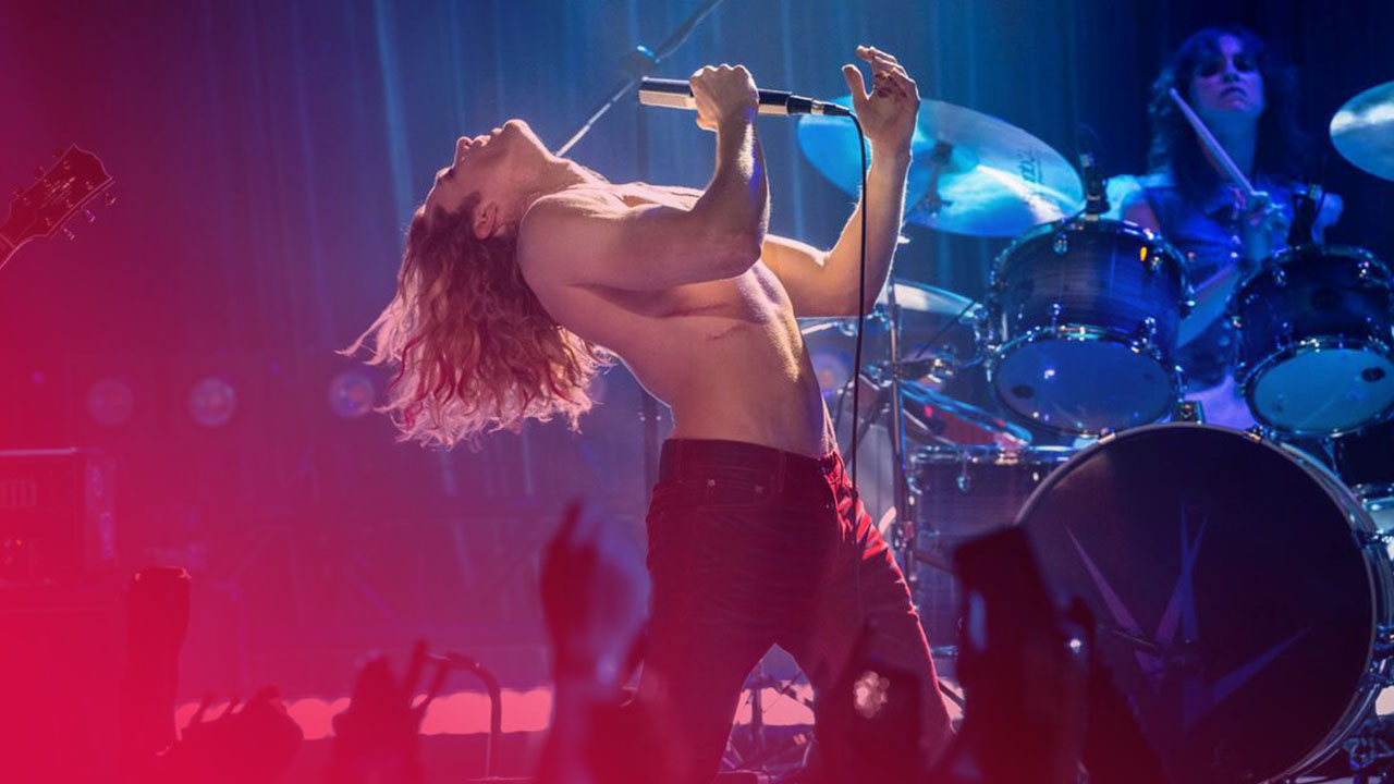 Ein unbekleideter Oberkörper eines langhaarigen Sängers, der sich auf einer blau beleuchteten Bühne nach hinten beugt und singt, während im Hintergrund ein Schlagzeuger spielt.