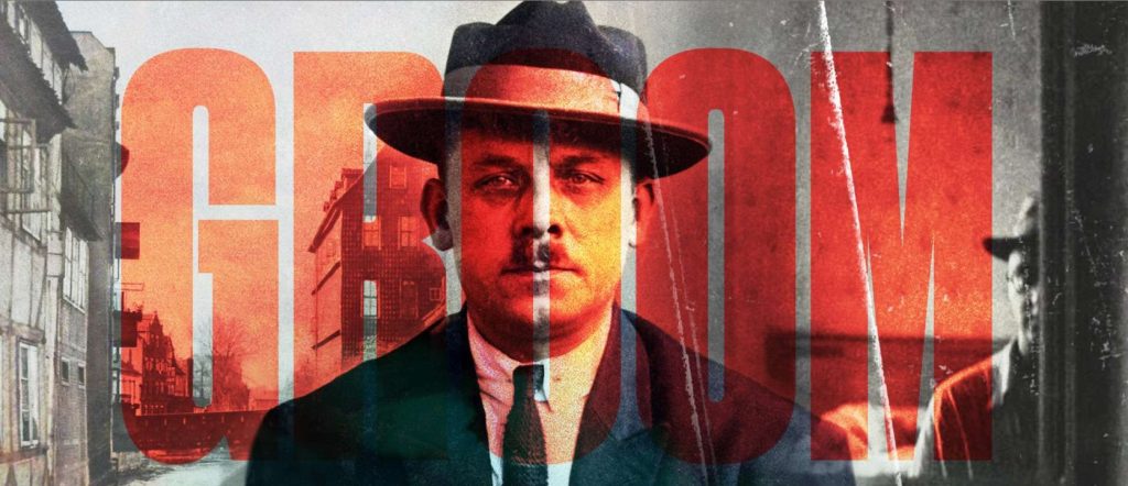 Ein Mann mit Hut und Anzug blickt ernst in die Kamera. Das Bild ist stilisiert mit roten Farbflächen und dem großen Schriftzug "GROOM" im Vordergrund, was eine düstere, historische Atmosphäre erzeugt.