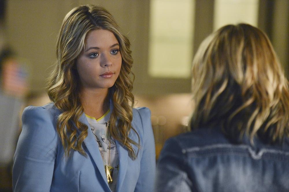 Eine junge Frau mit blonden, gewellten Haaren in einem hellblauen Blazer blickt ernst auf eine andere Person im Gespräch.