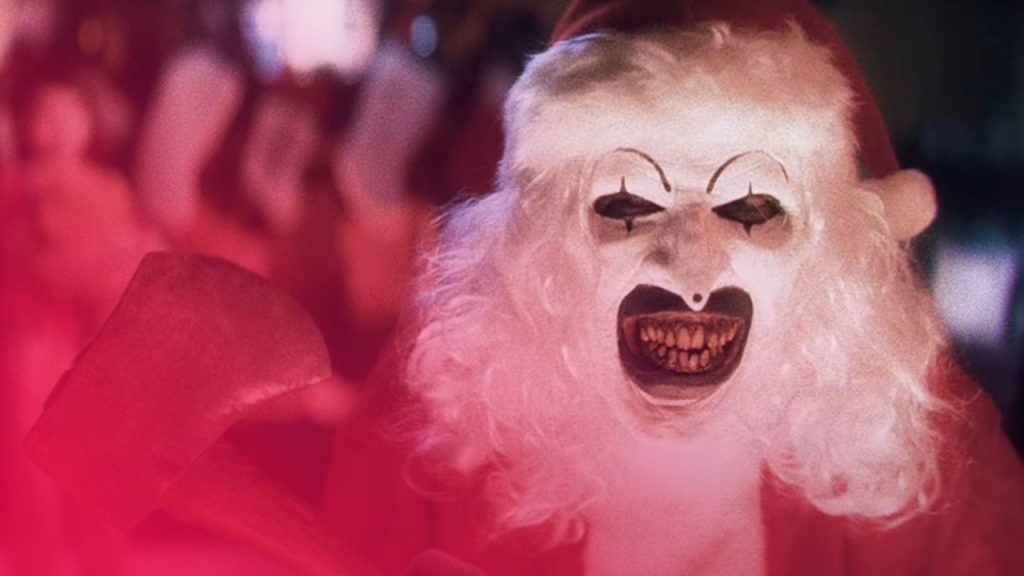 Eine Person in einem roten Weihnachtsmannkostüm mit weißer Perücke und einer gruseligen Maske mit schwarzem Mund und Augen hält eine Axt in der Hand.