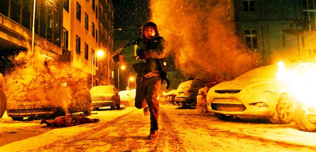 Eine Person rennt mit einem Koffer durch eine schneebedeckte Straße bei Nacht, während im Hintergrund eine heftige Explosion mit Feuer und Funken zwischen geparkten Autos stattfindet.