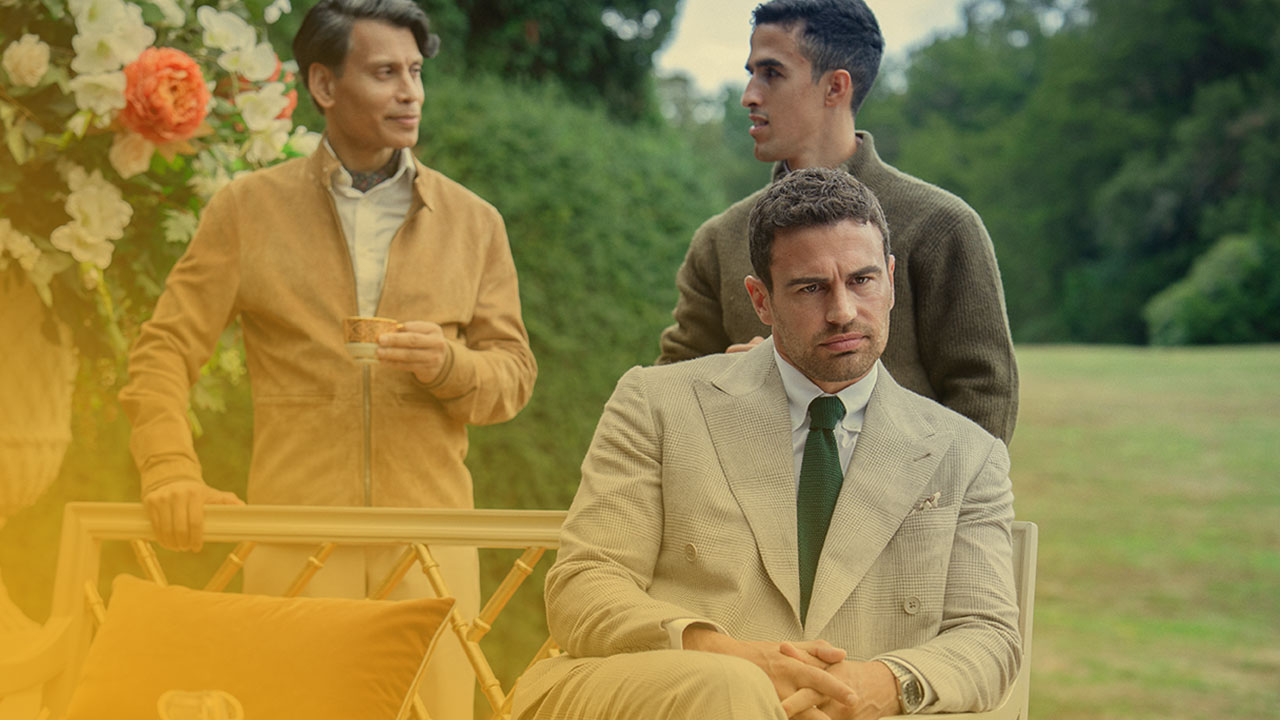 Drei Männer in eleganter Kleidung bei einer Gartenparty, einer sitzt im Vordergrund in einem hellen Anzug mit grüner Krawatte.